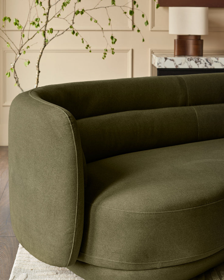 Henry 3-seater sofa in olive green velvet with curved arms, shown from angled side view in a styled living room setting.