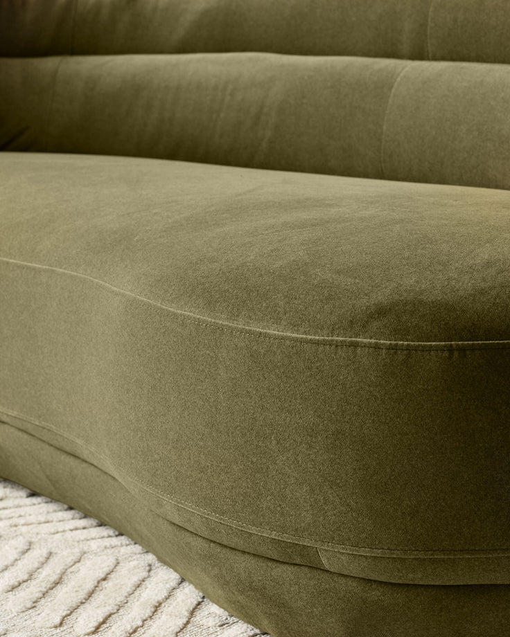 Close-up of Henry 3-seater sofa in olive green velvet, showing curved arm detail and seating surface with visible stitching.