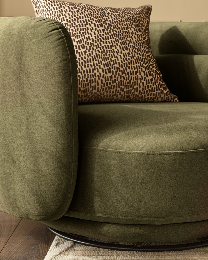 Henry swivel love seat in olive green velvet with patterned throw pillow, angled side view.
