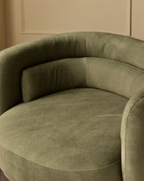 Henry swivel love seat in olive green velvet, curved design shown from side angle against cream wall.