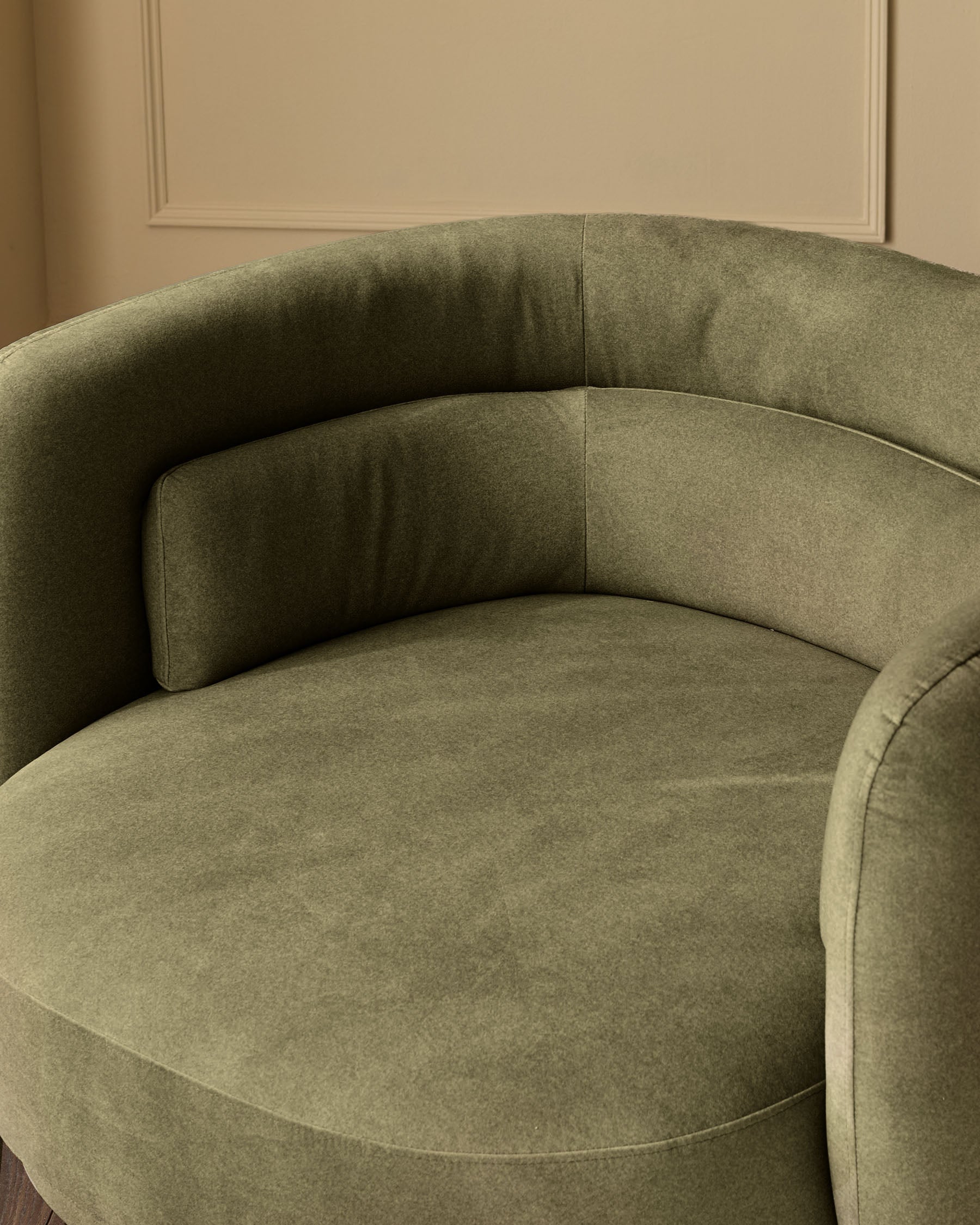 Henry swivel love seat in olive green velvet, curved design shown from side angle against cream wall.