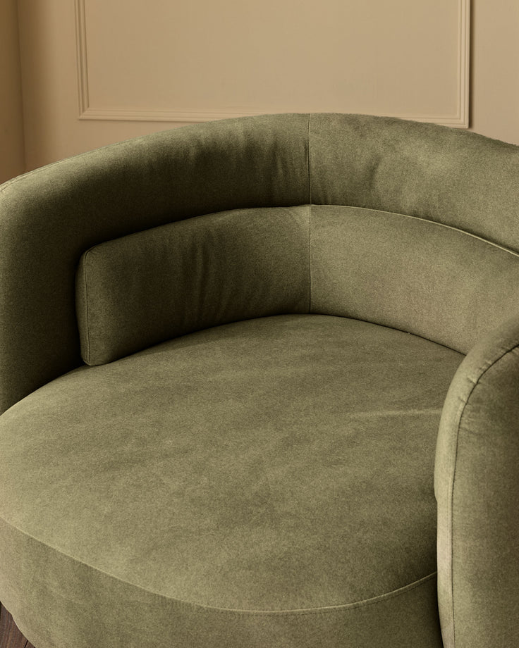 Henry swivel love seat in olive green velvet, curved design shown from side angle against cream wall.