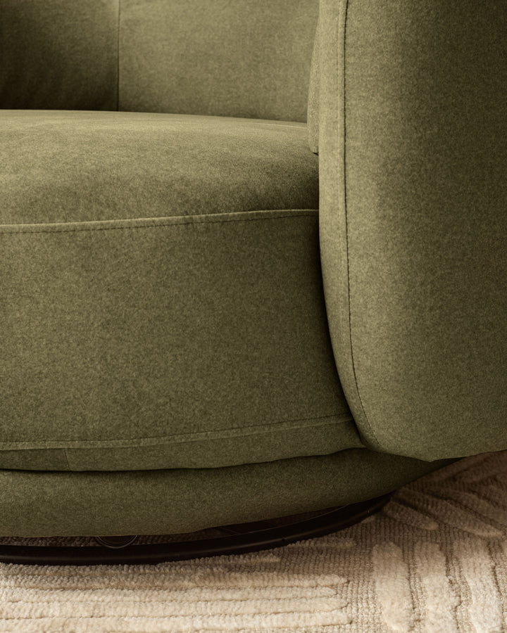 Henry swivel love seat in olive green velvet, showing curved armrest and seating detail on neutral rug.