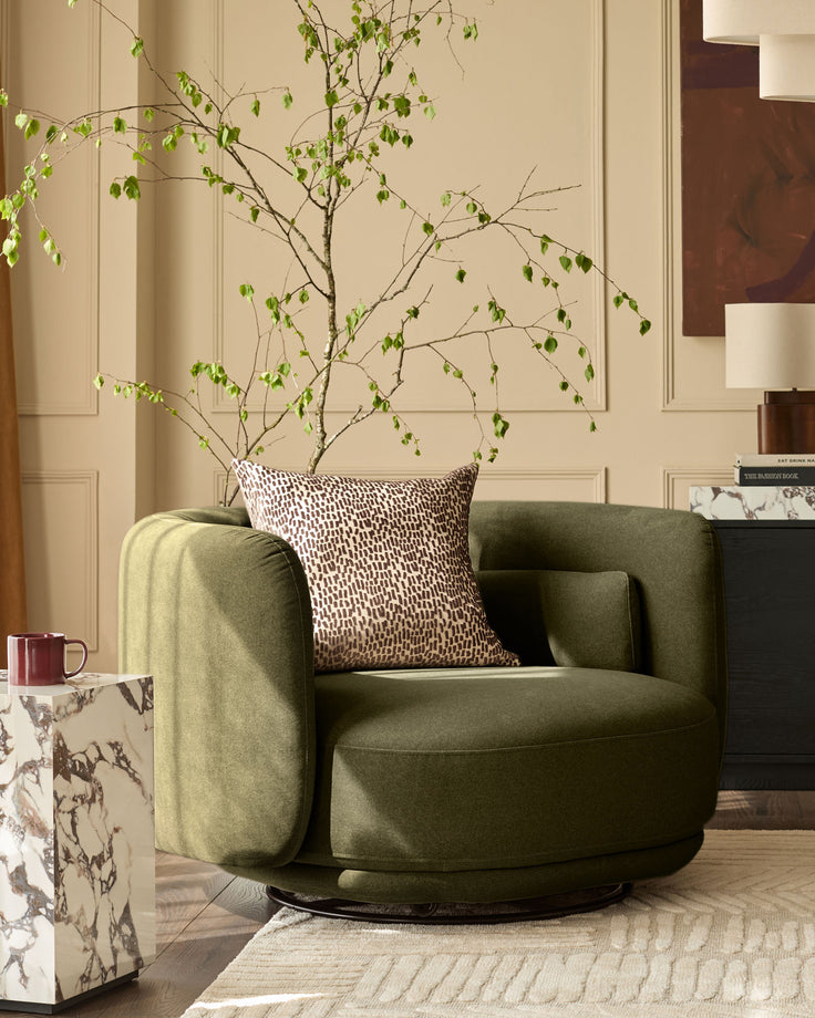 Henry swivel love seat in olive green velvet, shown in a styled living room setting with decorative pillow and potted plant.