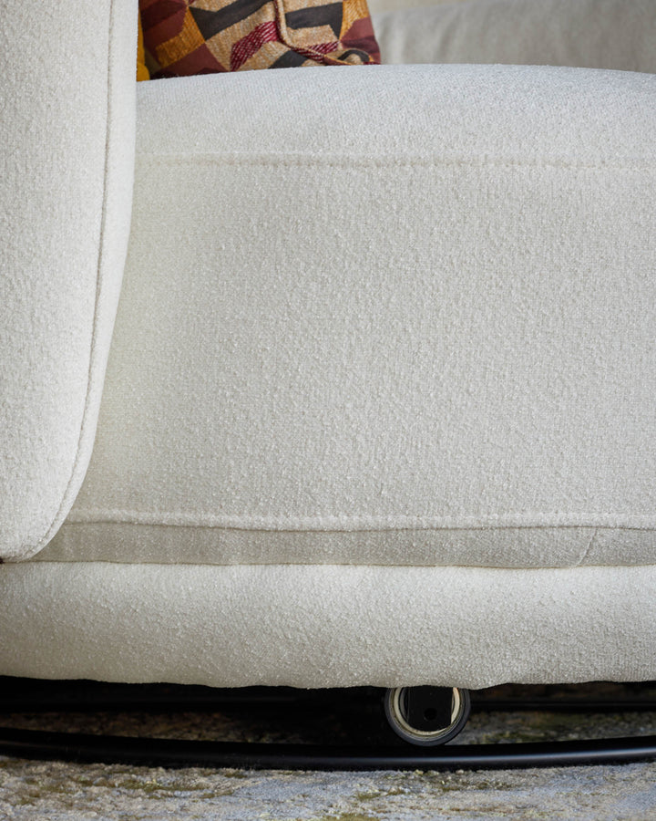 Close-up of a cream sofa with a patterned cushion. The sofa has a low profile and a soft, textured fabric.