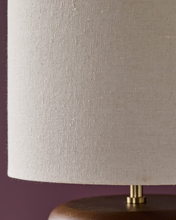 Hepworth table lamp with dark wood base and natural linen cylindrical shade, brass hardware detail visible.