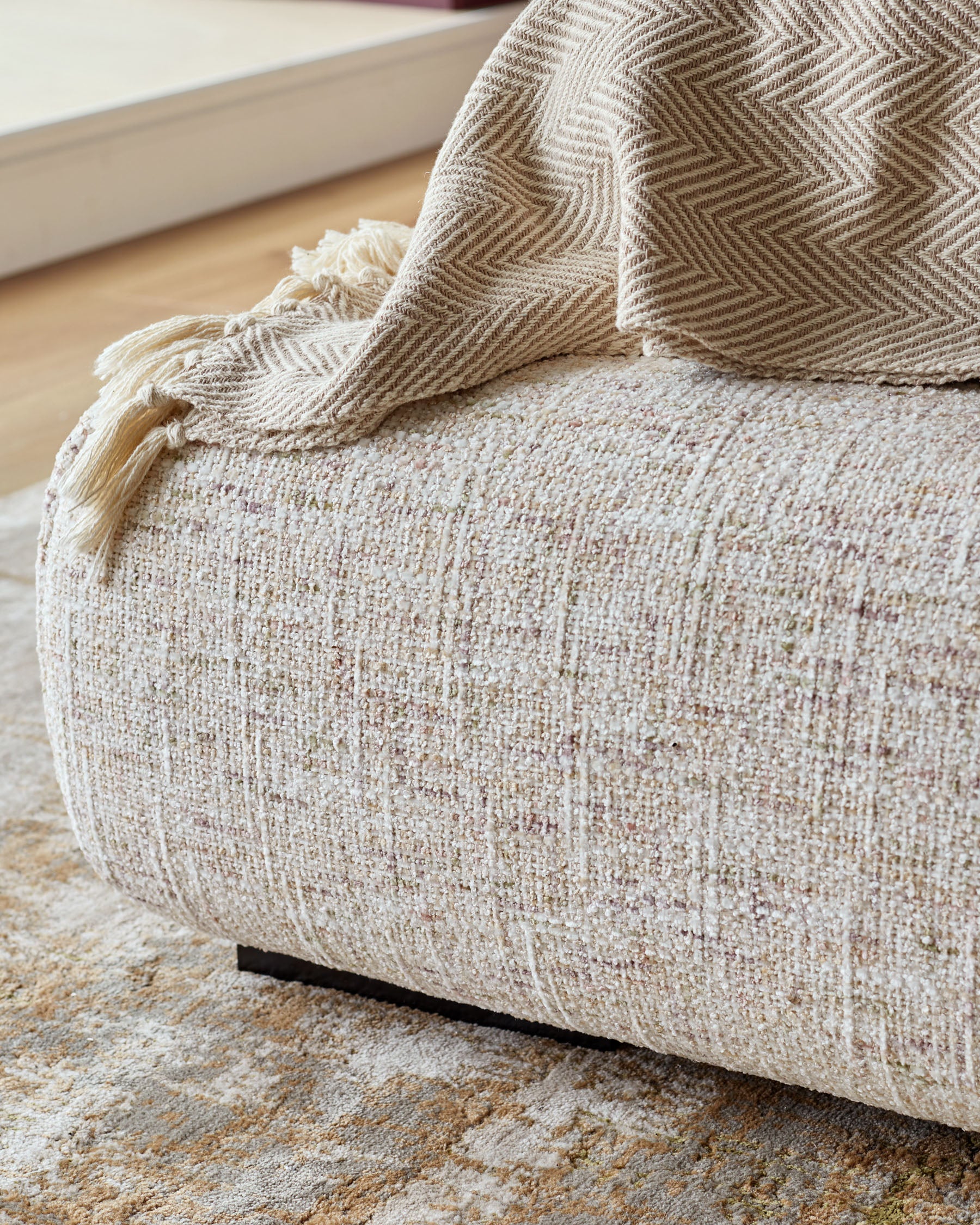 Hepworth king-size ottoman bed in natural fabric with tassel throw, close-up of textured upholstery and wooden leg detail.