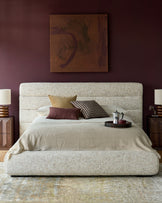 Hepworth King-Size Ottoman Bed in natural fabric with rounded edges, styled in a burgundy bedroom with pillows and bedding.