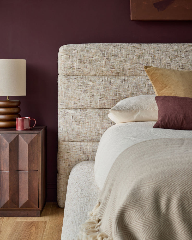 Hepworth king-size ottoman bed with natural linen upholstery, displayed in bedroom setting with neutral bedding and burgundy accent wall.