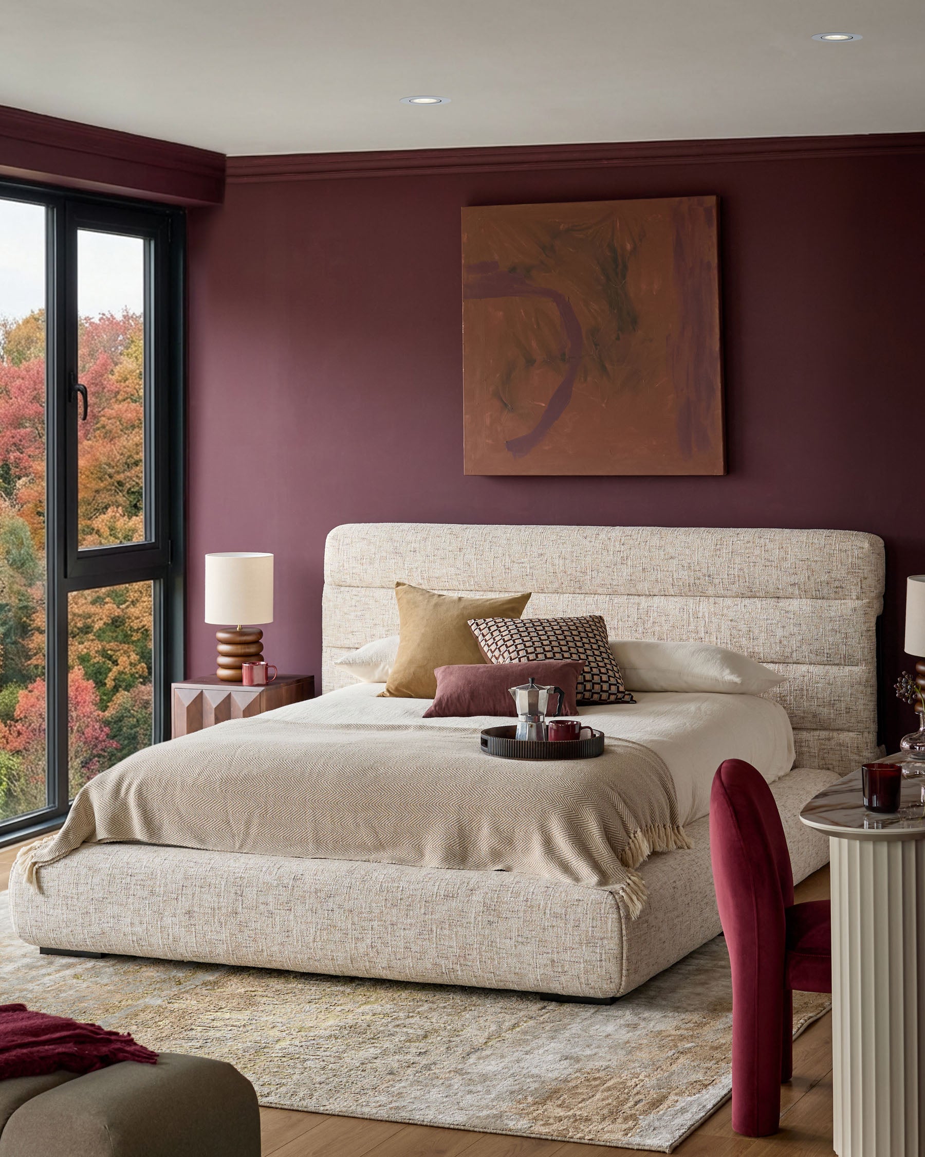 Hepworth King-Size Ottoman Bed in natural fabric, displayed in a burgundy bedroom with cream bedding and decorative pillows.