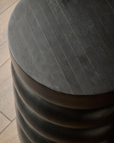 Black mango wood side table with curved cylindrical design and natural wood grain texture visible on top.