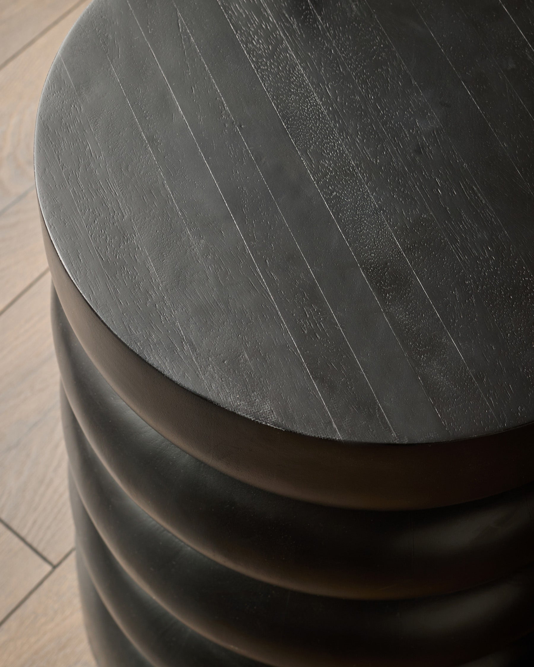 Black mango wood side table with curved cylindrical design and natural wood grain texture visible on top.
