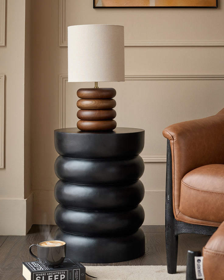Black stacked side table with mango wood lamp base in contemporary living room setting.