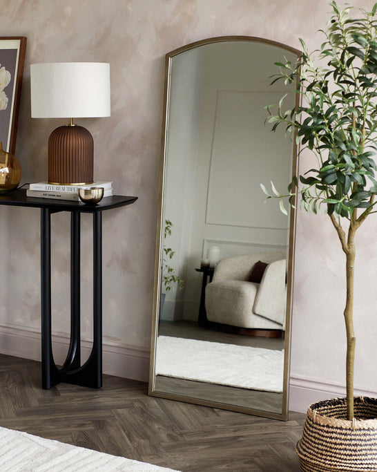 Elegant slim console table with a sleek black metal frame and a glossy tabletop, accompanied by a tall arch-shaped full-length mirror with a minimalist bronze frame.