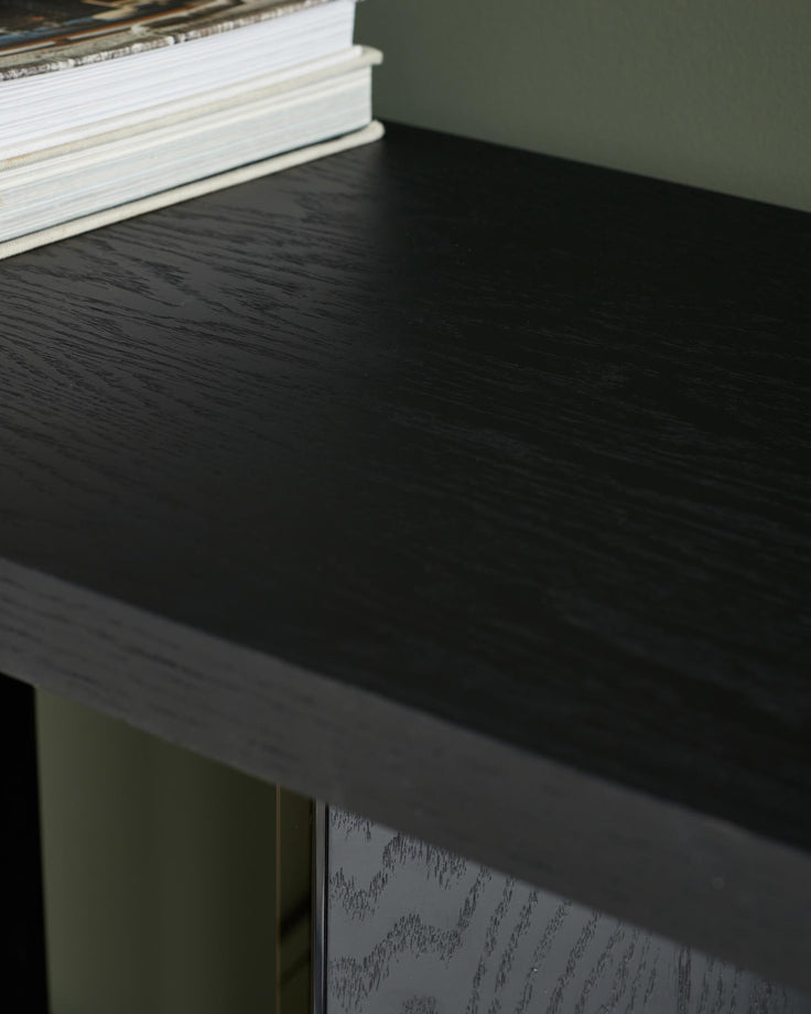 Close-up of a black wood sideboard with books on top, highlighting the wood grain and finish.