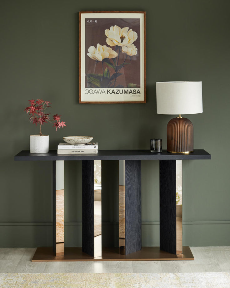 Console table in dark wood and brushed bronze, styled with a lamp, plant and books against a dark green wall.