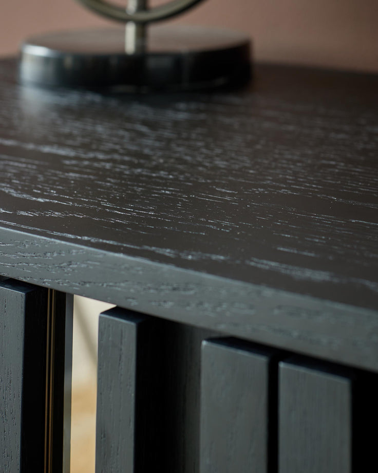 Close-up of a dark wood table with vertical slat detailing. A modern and minimalist piece of furniture.
