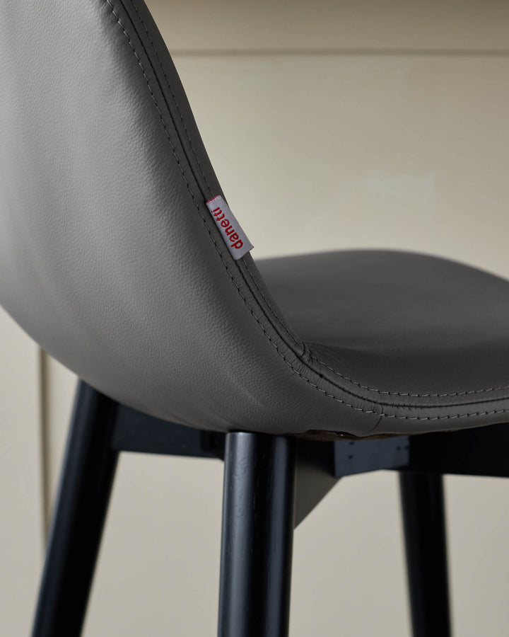 Close-up of a grey leather chair with black legs, featuring a 'danetti' tag on the backrest.