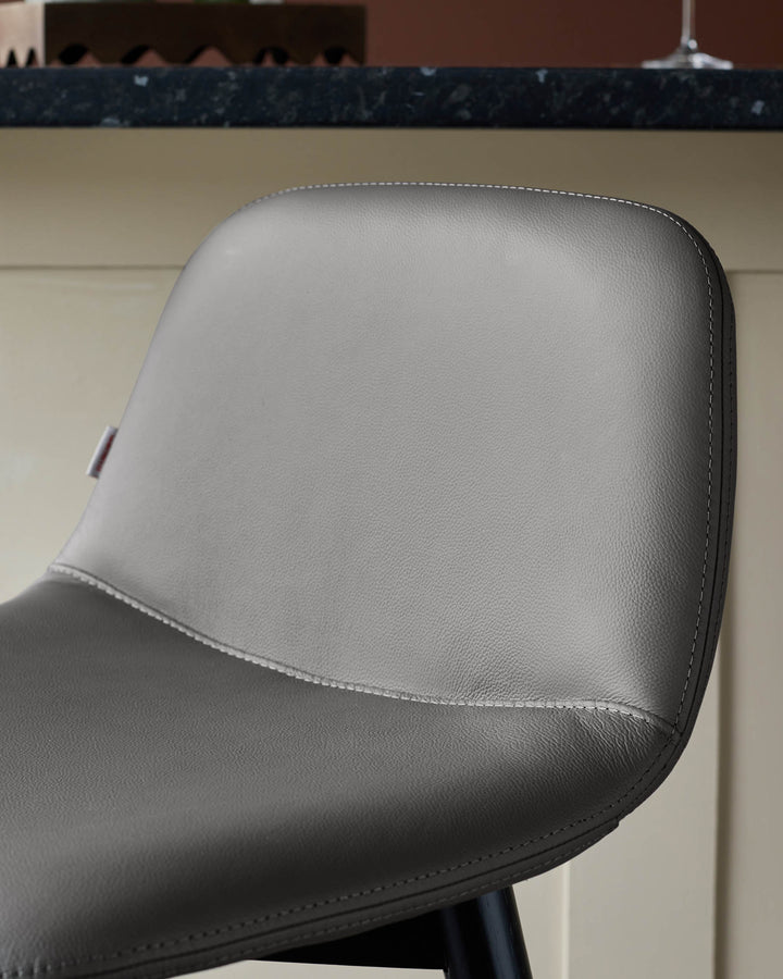 Close-up of a stylish grey leather bar stool with a subtle stitch detail. Ideal for modern kitchen and dining spaces.