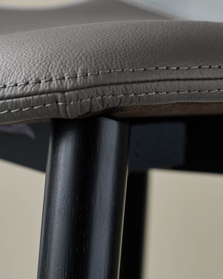 Close-up of a grey leather seat with black wooden legs. Modern design and craftsmanship.