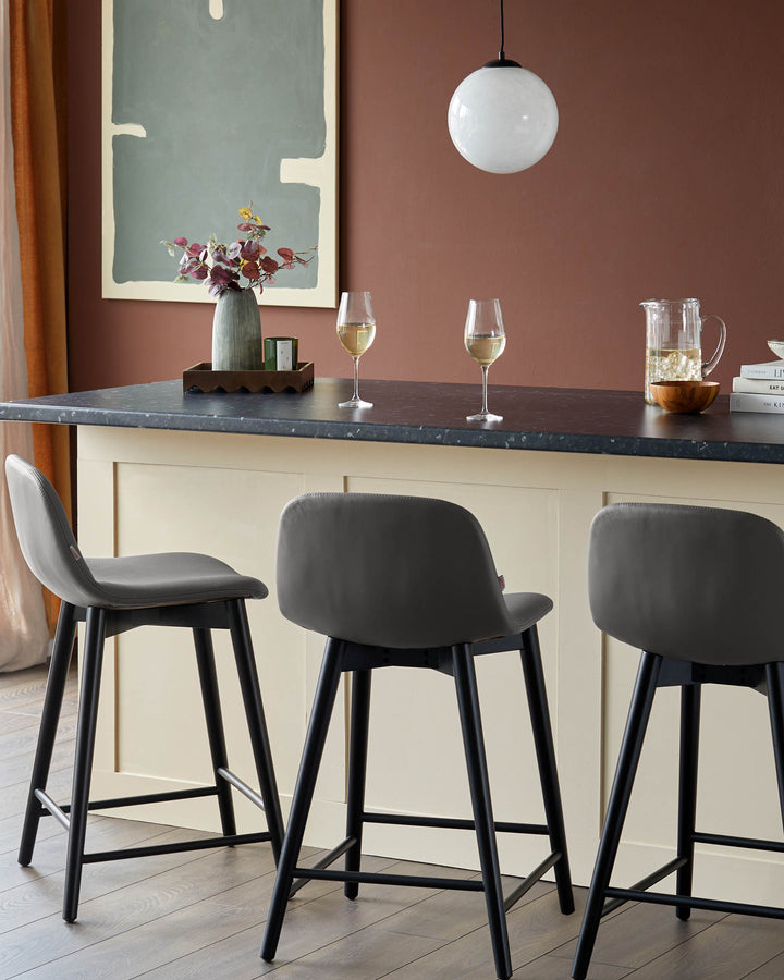 Contemporary kitchen with three grey bar stools, black legs, a counter, and stylish decor.