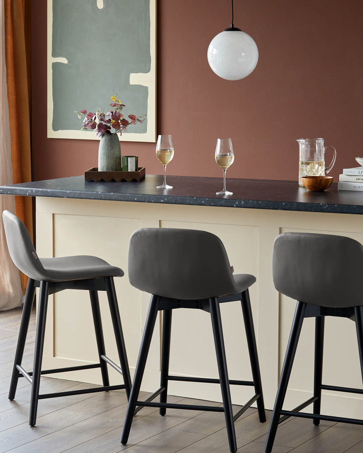 Contemporary kitchen with three grey bar stools, black legs, a counter, and stylish decor.