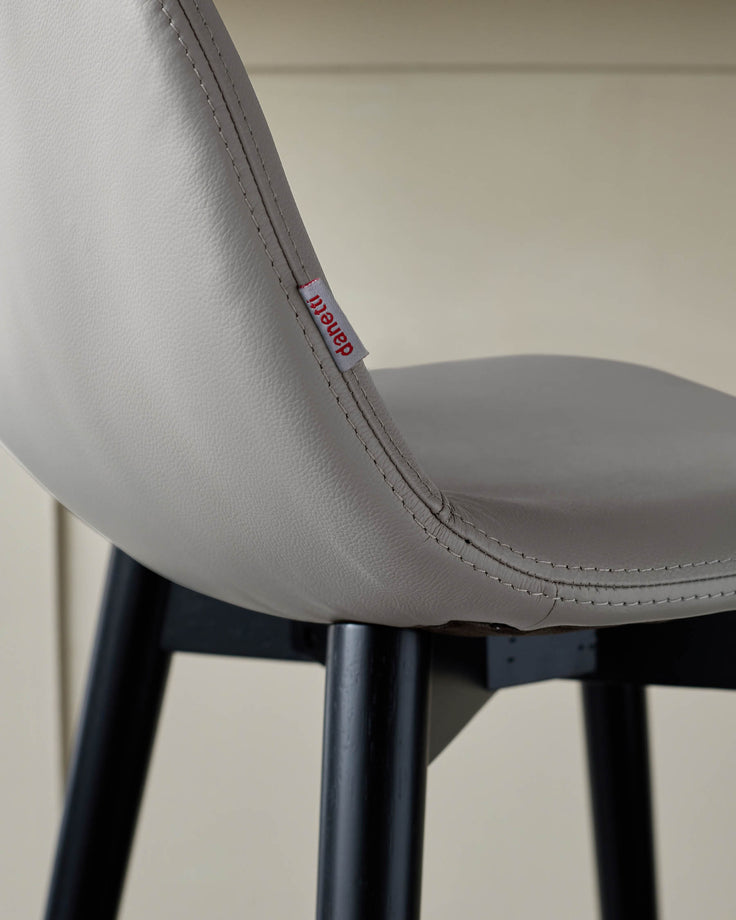 Close-up of a stylish, grey faux leather chair with black legs and a subtle 'danetti' brand tag.