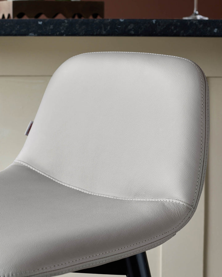 Close-up of a grey faux-leather bar stool with a contoured seat and back, with subtle stitching details.