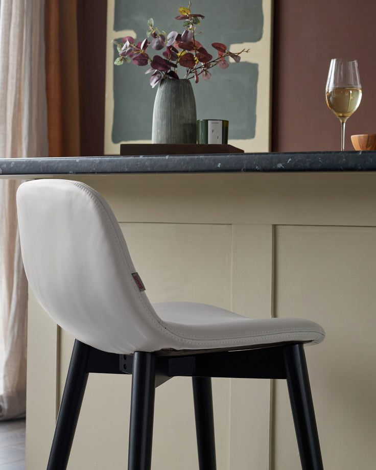 Stylish bar stool with pale leather seat and black legs, positioned at a kitchen island. Contemporary design and neutral colour palette.