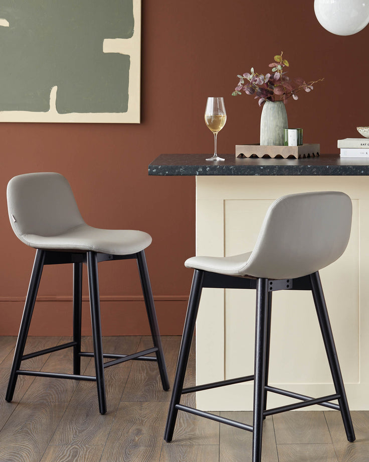 Two grey bar stools with black legs sit beside a kitchen island, adding a touch of modern elegance to the space.