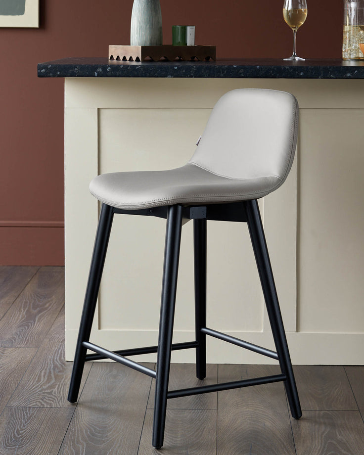 A modern stool with black legs and a beige seat, positioned in front of a counter in a warm, inviting room.