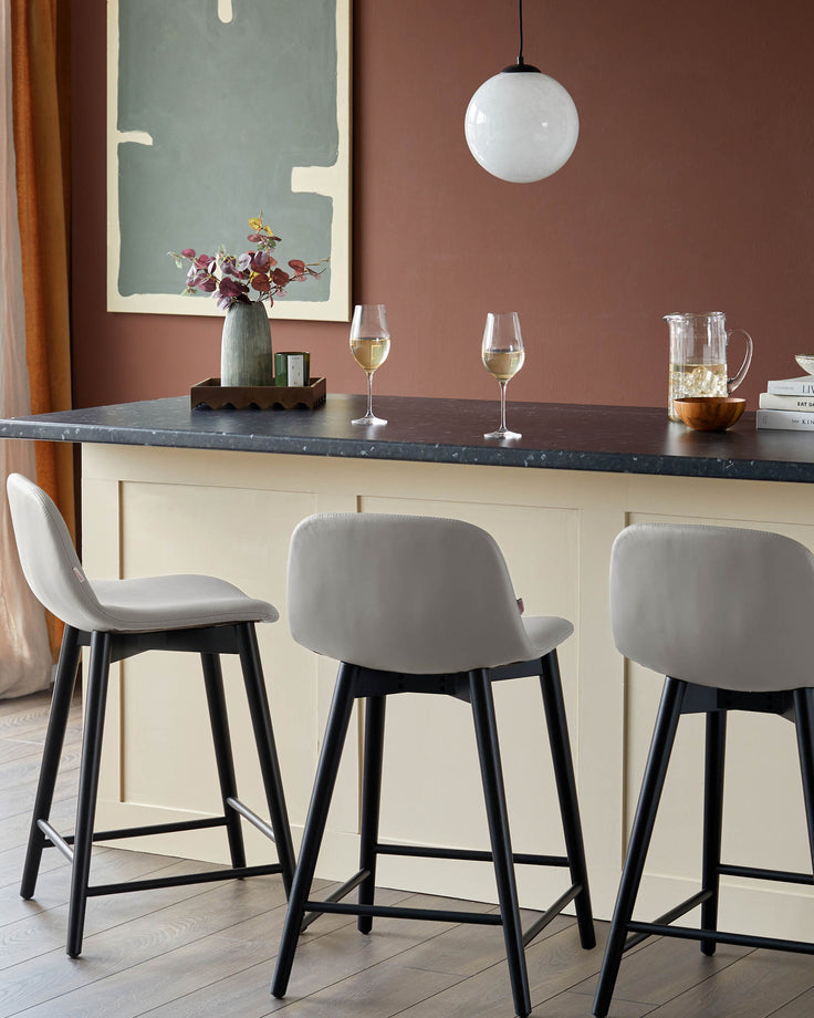 Three modern bar stools with grey seats and black legs at a kitchen island.