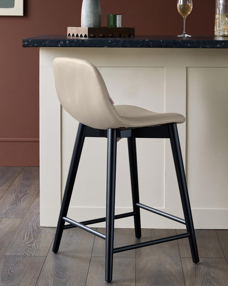 A sleek bar stool with a beige seat and black legs sits stylishly in front of a kitchen island, adding a touch of modern sophistication.