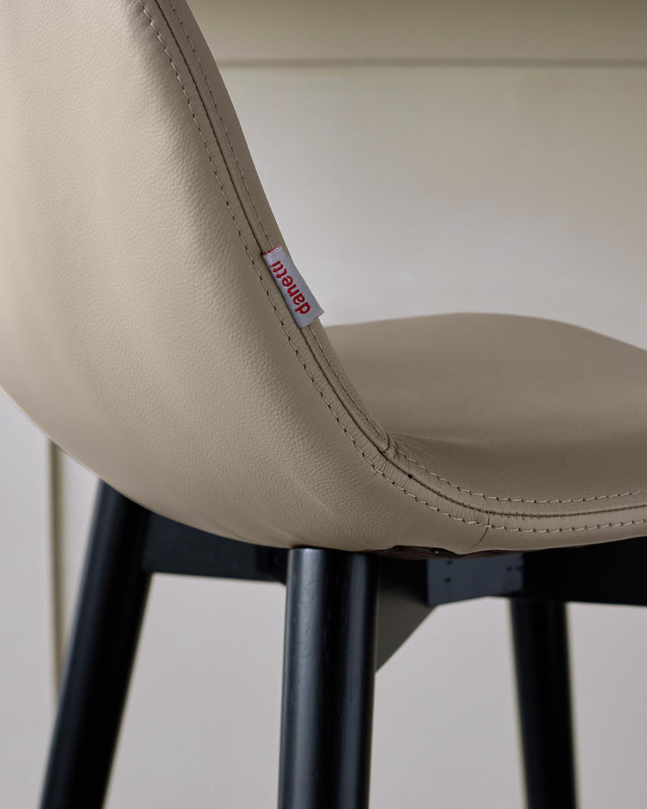 Close-up of a chair featuring a beige leather seat and black legs, showcasing simple and elegant furniture design.
