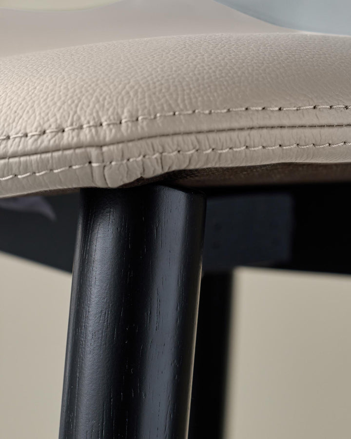 Close-up of a modern chair. Features a beige padded seat and a dark wood leg for a stylish touch.
