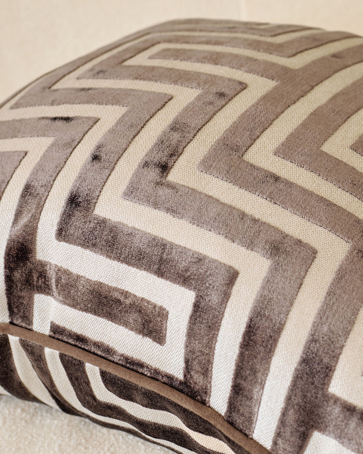 Chocolate brown and cream chevron patterned cushion with piping detail, angled close-up view.