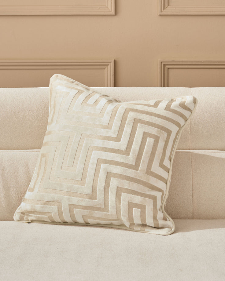 Imani cushion in ivory with geometric tan and cream striped pattern, displayed on a beige upholstered sofa.
