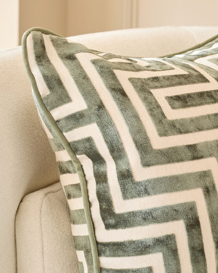 Imani cushion in olive green and cream with geometric maze pattern, draped over cream upholstered chair arm.