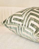 Imani cushion in medium olive green with white geometric stripe pattern, shown at an angle on a neutral surface.