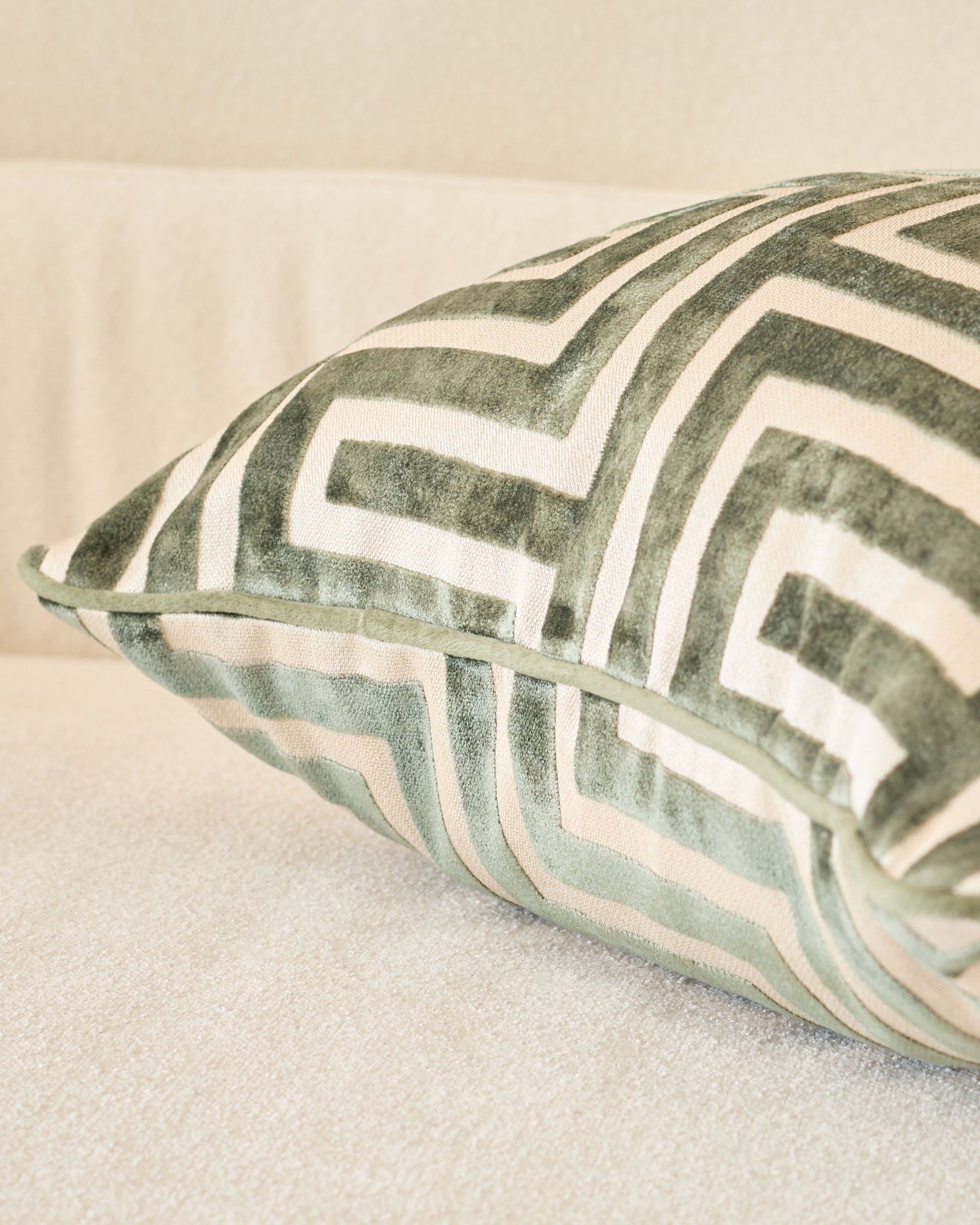 Imani cushion in medium olive green with white geometric stripe pattern, shown at an angle on a neutral surface.