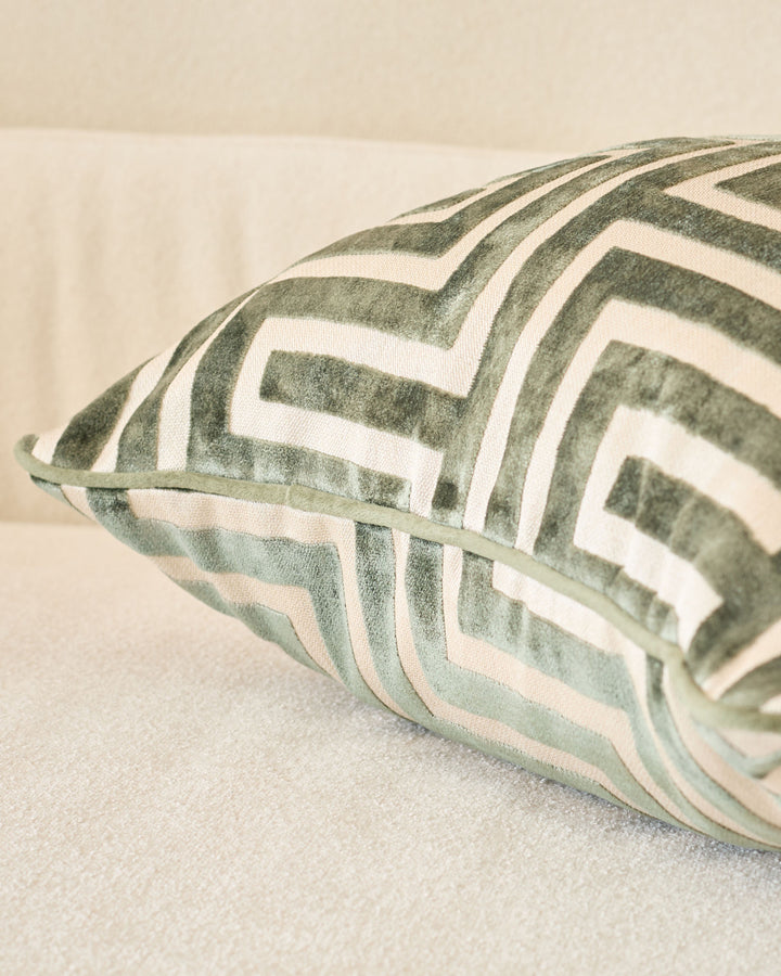 Imani cushion in medium olive green with white geometric stripe pattern, shown at an angle on a neutral surface.