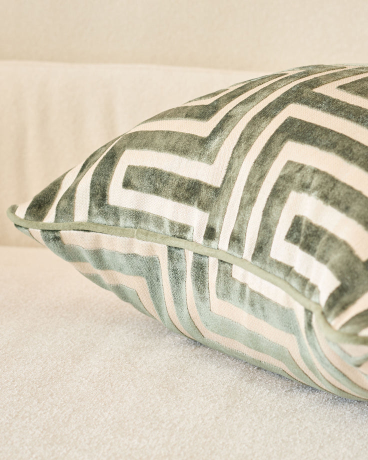Imani cushion in medium olive green with white geometric stripe pattern, shown at an angle on a neutral surface.