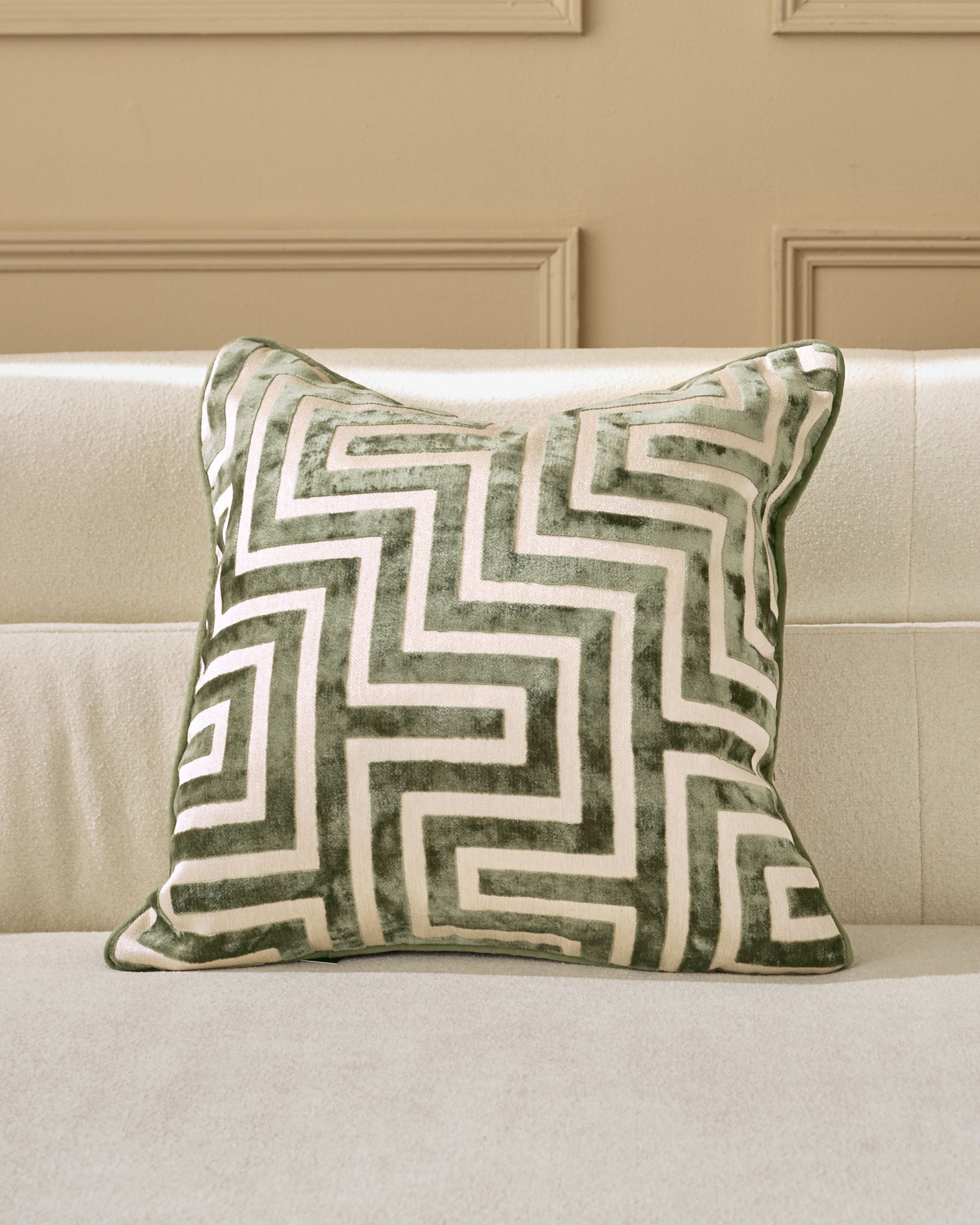 Imani cushion in medium olive green with cream geometric pattern, displayed on a beige sofa.