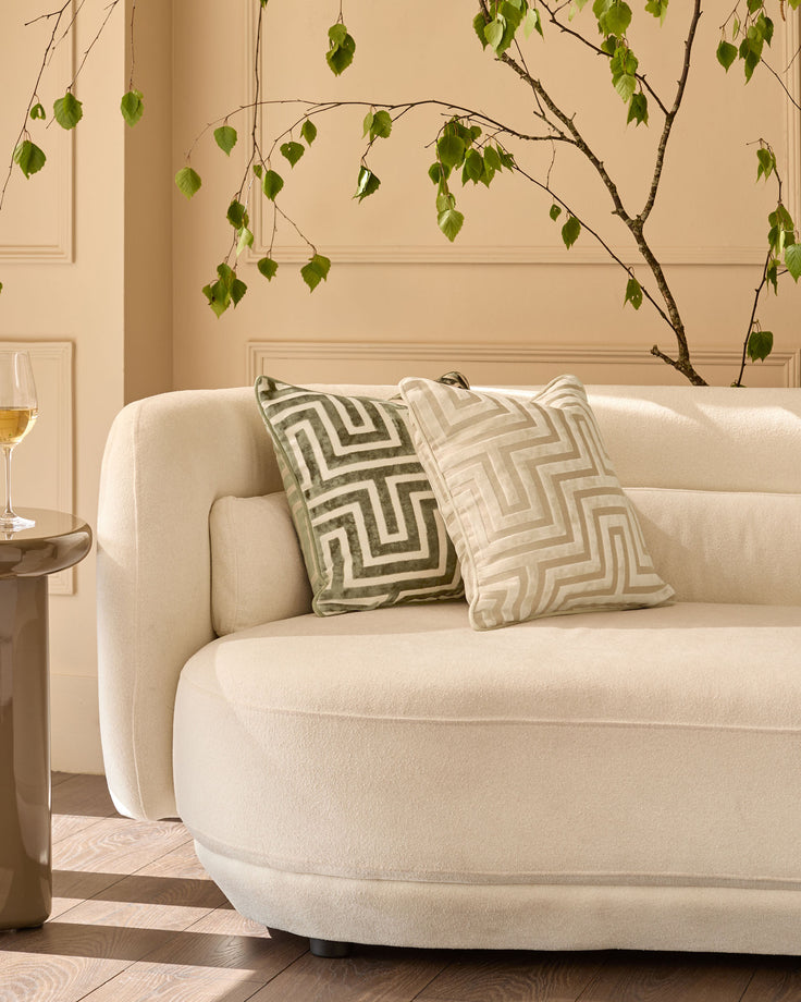 Imani Cushion in Medium Ivory with geometric pattern, displayed on cream curved sofa in modern living room setting.