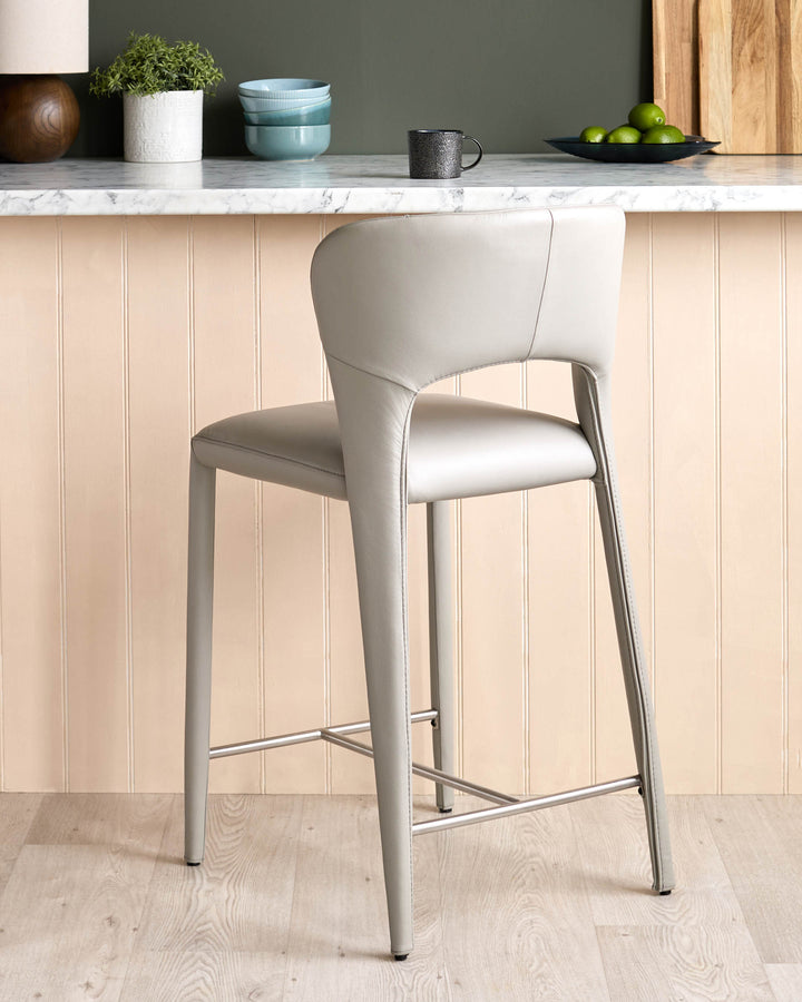 Light grey leather bar stool with curved backrest and metal footrest, positioned at marble countertop.