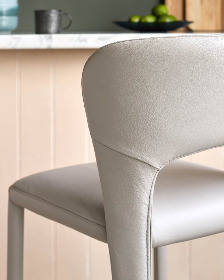 Light grey leather bar stool with curved backrest and sleek leg design, shown in close-up detail.