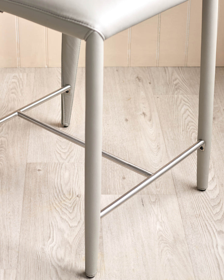Jackson bar stool with chrome footrest and leg detail, light grey leather seat, modern design on light wood floor.