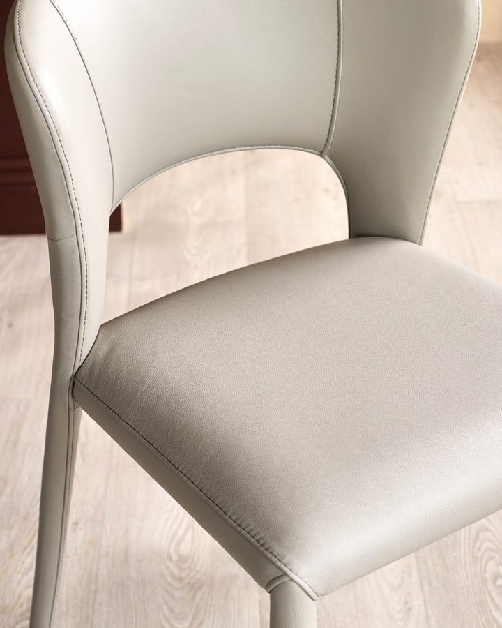 Jackson dining chair in light grey real leather, shown at an angle highlighting the curved backrest and stitched seams on a wooden floor.