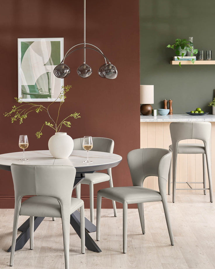 Jackson dining chair in light grey real leather, shown in a dining room setting with round white table and terracotta accent wall.