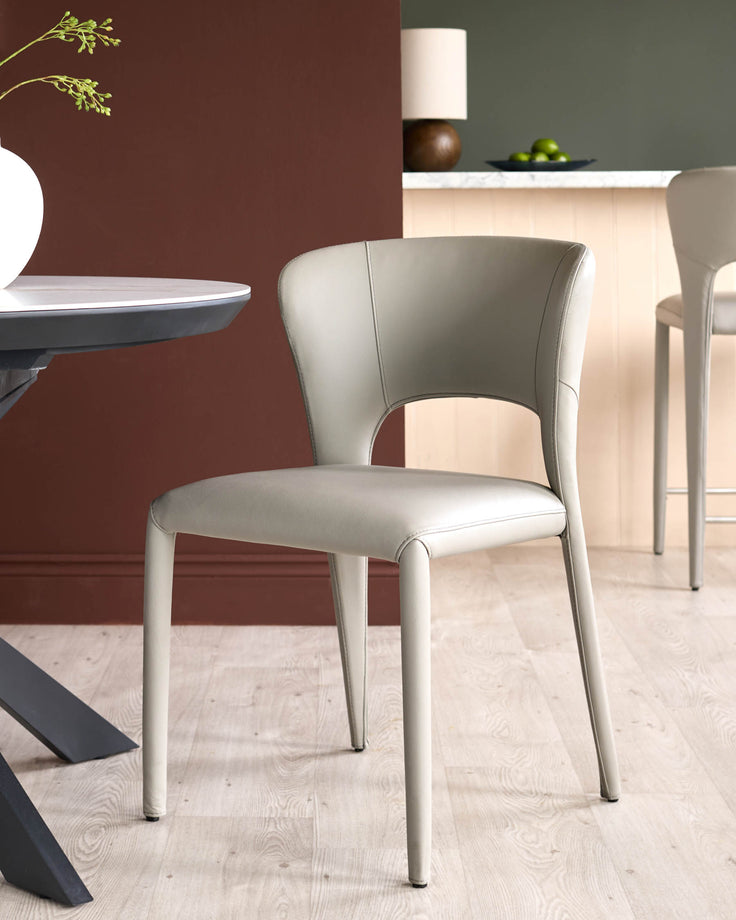 Jackson dining chair in light grey real leather, shown in a modern dining space with curved backrest and sleek legs.